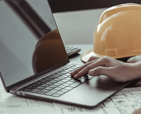 Side view of person typing on laptop with hard hat in the background