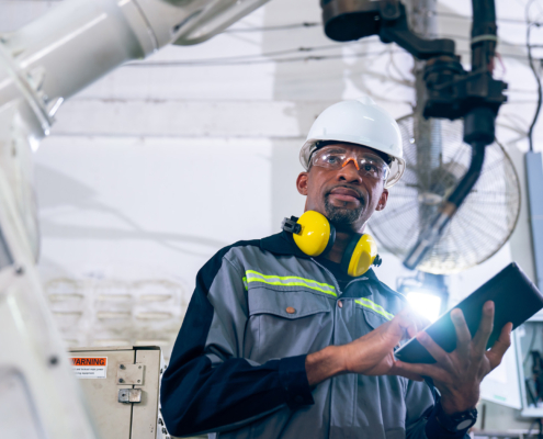 Front view of engineer with tablet in hard hat looking at factory equipment